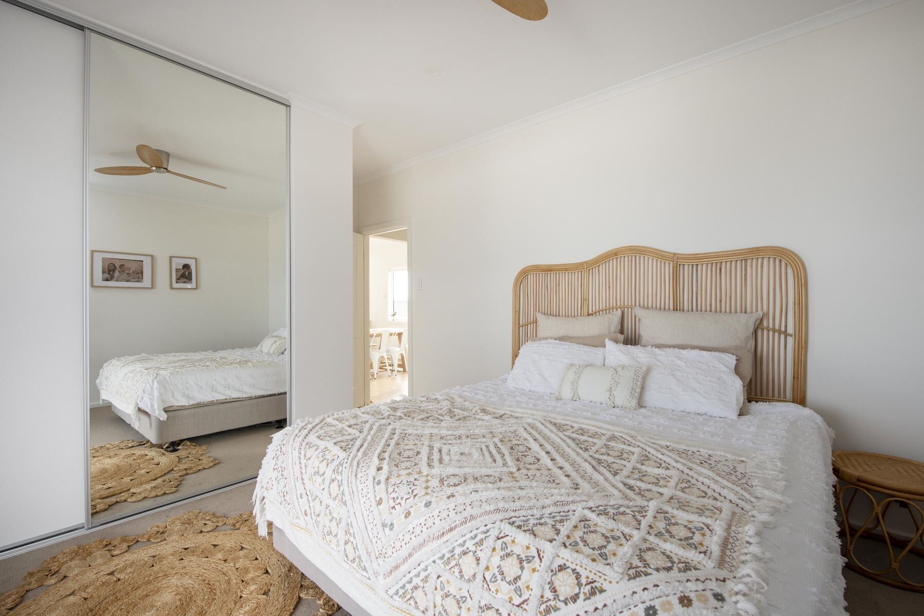 Une chambre avec un grand miroir, un lit recouvert d’une couverture tissée, une tête de lit en bois et une petite table de chevet en bois.