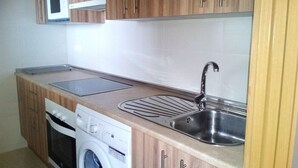 A compact kitchen with wooden cabinets, a microwave, a sink, and a washing machine. - Torre De La Roca (Torremolinos)
