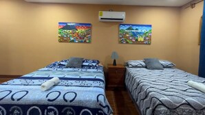 Hotelkamer met twee bedden, een nachtkastje, een airconditioner en twee aan de muur bevestigde schilderijen.