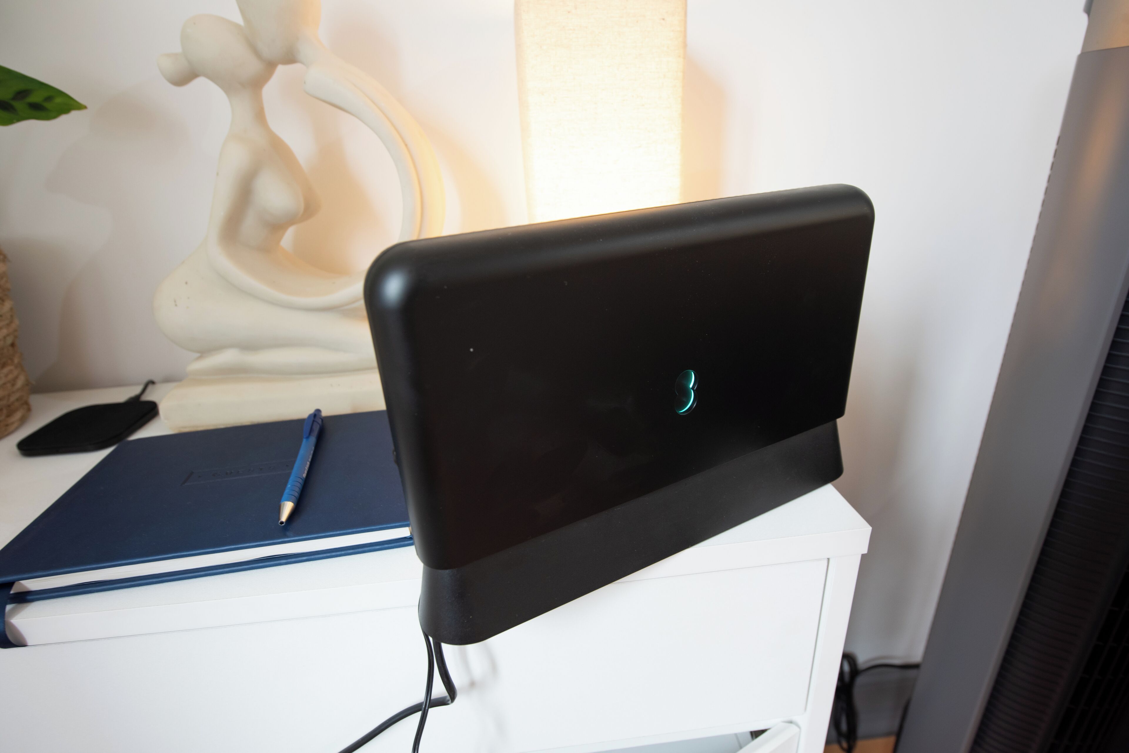 A laptop on a white desk with a blue notebook and a pen.