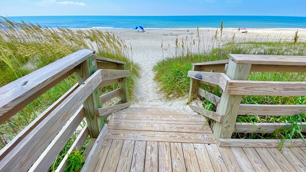 A wooden boardwalk leading to a beach with a clear view of the ocean and beachgoers.