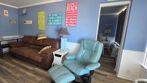 A living room with a brown sofa, teal armchair, and a small table with a lamp.