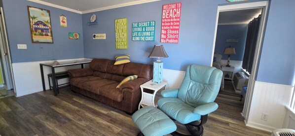Un salon avec un canapé marron, un fauteuil turquoise et une petite table avec une lampe.