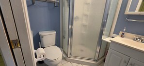 Un baño con inodoro, cabina de ducha y lavabo con dispensador de jabón.