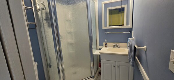 A bathroom with a glass shower door, a sink, a mirror, and a towel rack.