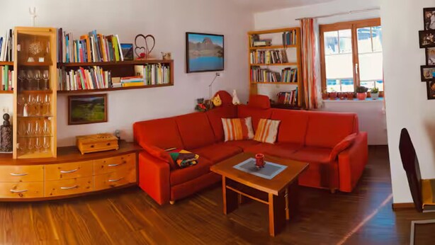 Ein gemütliches Wohnzimmer mit einem roten Sofa, einem Holztisch und Bücherregalen voller Bücher und Dekoration.