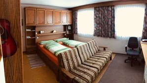 Ein Schlafzimmer mit einem Bett, einem Schreibtisch, einem Stuhl und einer Gitarre.