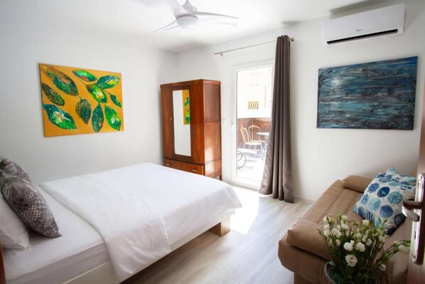 A hotel room with a bed, a sofa, a mirror, and two paintings.