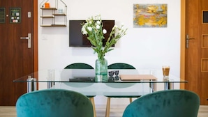 Un comedor moderno con una mesa de vidrio, sillas color turquesa, un jarrón con flores blancas, un estante con objetos decorativos y un cuadro en la pared.