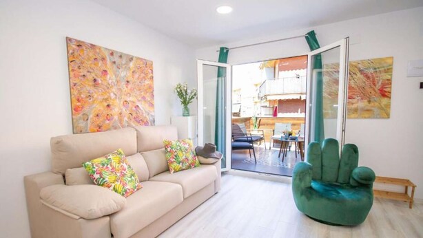 Un salón con un sofá color beige, un sillón verde y dos cuadros abstractos.