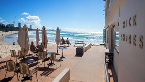 A beachfront patio with tables and chairs, umbrellas, and a view of the ocean.