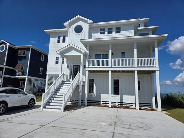 A two-story white building with a balcony, a staircase, and a car parked in front.