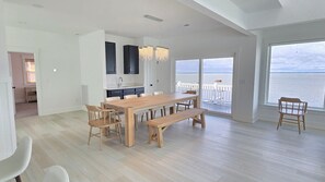 A spacious living area with a wooden dining table, benches, and a view of the sea through large windows.
