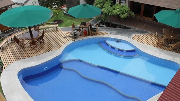 A swimming pool with a wooden deck, surrounded by outdoor furniture and umbrellas.