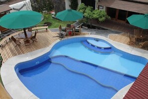 A swimming pool with a wooden deck, surrounded by outdoor furniture and umbrellas.