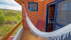 A balcony with a white hammock, a red chair, and a view of greenery.