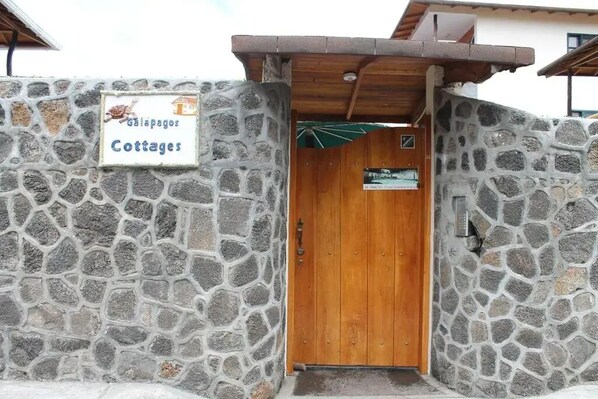 A stone wall with a wooden door and a sign reading "Galapagos Cottages".