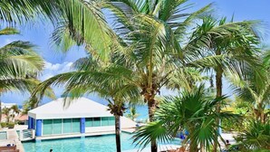 A pool area with palm trees, lounge chairs, and a building with large windows. - Seaside Condo by Solymar (Cancun)