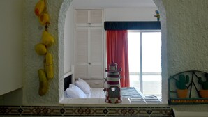 A room with a bed, a window with red curtains, a lighthouse decoration, and a cactus plant. - Seaside Condo by Solymar (Cancun)