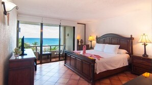A hotel room with a large bed, a desk with a lamp, a chair, and a view of the ocean. - Seaside Condo by Solymar (Cancun)