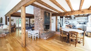 Amplia sala de estar con techo de madera, chimenea de ladrillo y cocina al fondo.