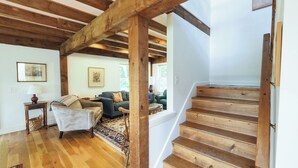 Una escalera de madera que conduce a un segundo piso, una sala de estar con un sofá y una mesa de centro, y una alfombra estampada en el suelo.