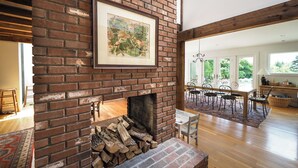 Amplia sala de estar con chimenea de ladrillo, una mesa de comedor con sillas y vistas al exterior.