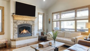 A living room with a stone fireplace, a sofa, a coffee table, and large windows.