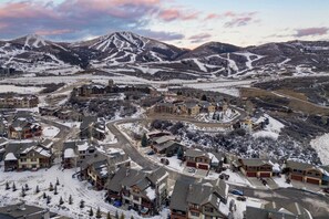 Un pueblo cubierto de nieve con edificios residenciales, una carretera sinuosa y montañas al fondo.