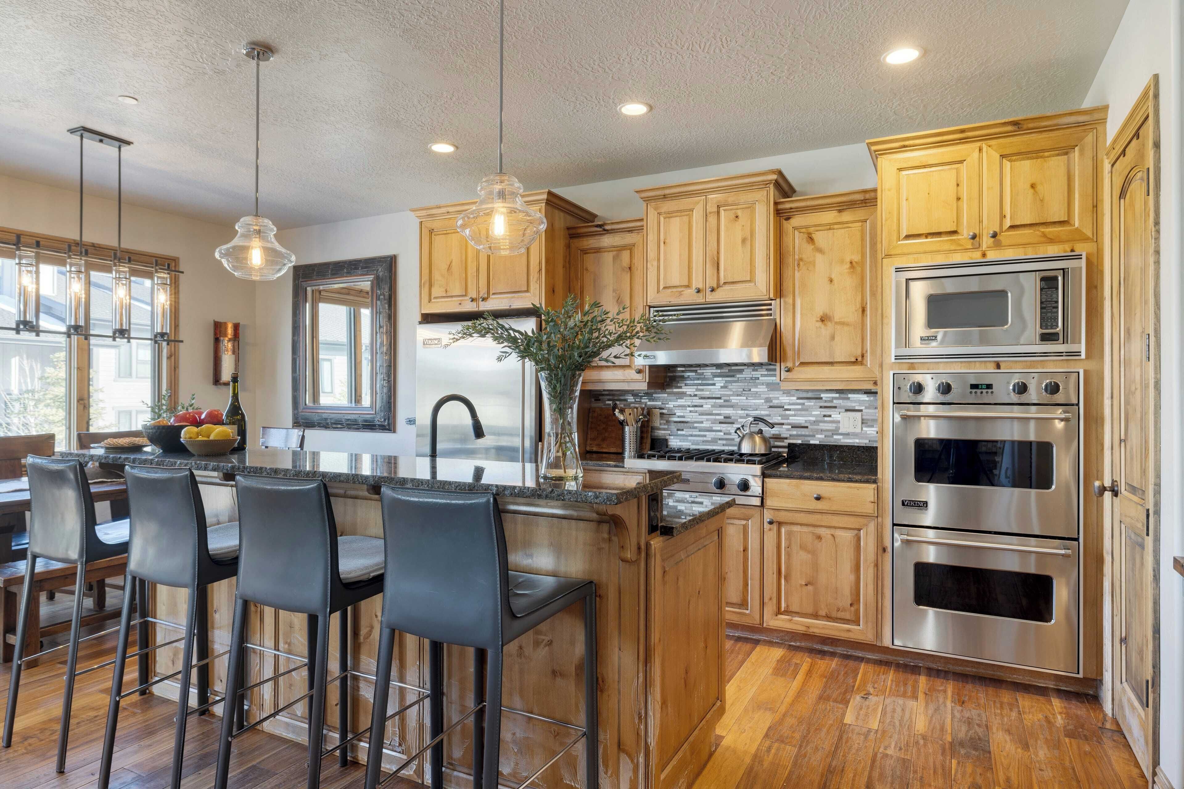 A modern kitchen with wooden cabinets, stainless steel appliances, and a bar area with stools.