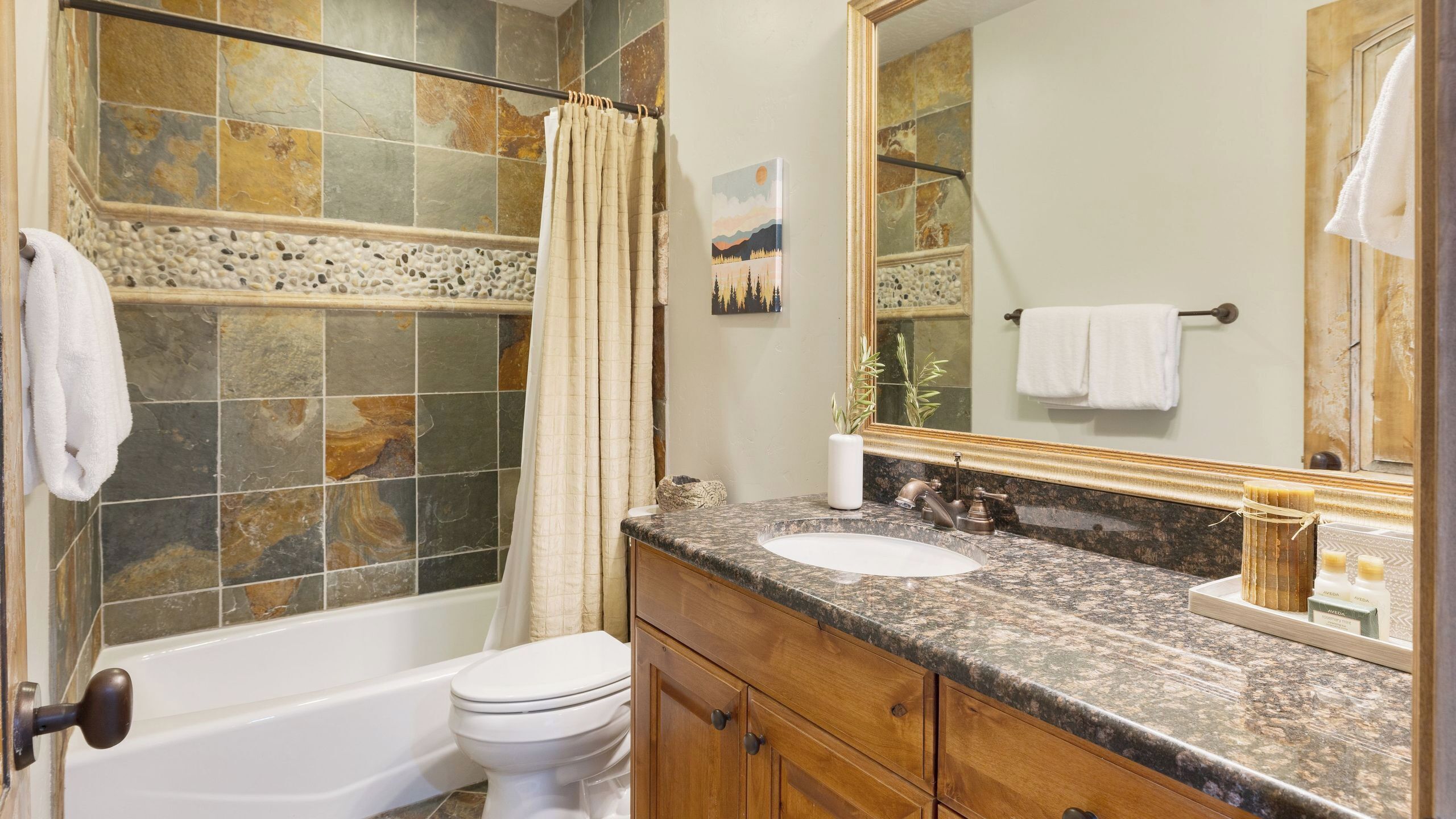 A bathroom with a bathtub, toilet, vanity with a sink, and a large mirror.