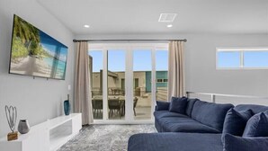 Una sala de estar moderna con un sofá grande azul, un mueble blanco para entretenimiento y un ventanal corredizo que da a un patio exterior.