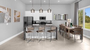 Cocina moderna con una isla central, taburetes de bar e iluminación colgante.