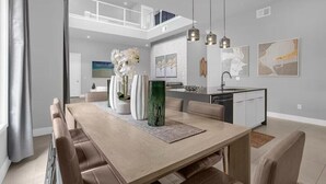 Un comedor moderno con techo alto, iluminación colgante y obras de arte en las paredes.