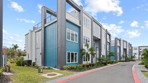 A modern multi-story residential building with a blue and grey facade, a curved driveway, and landscaped gardens.