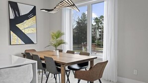 A modern dining area with a wooden table and chairs, a potted plant, and a large abstract painting on the wall.