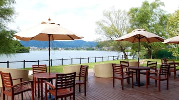 Un espacio al aire libre con mesas y sillas, sombrillas y vistas a un lago y montañas.