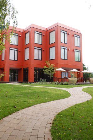 A red building with multiple windows and a paved pathway leading to outdoor seating. - Hotel & Lakehouse Soka (Kyotango)