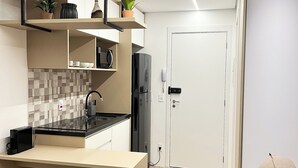 A modern kitchen with a black countertop, white cabinets, and a built-in oven. There is a small round stool and a beige sofa in the living area. - Studio sofisticado 230m do metrô (São Paulo)