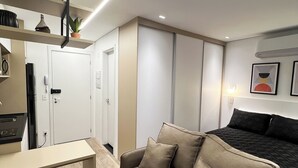 A modern, well-lit room with a sofa, a small table, and a kitchenette area. - Studio sofisticado 230m do metrô (São Paulo)
