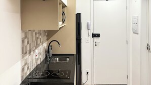 A modern kitchen with black appliances, a tiled backsplash, and a white door. - Studio sofisticado 230m do metrô (São Paulo)