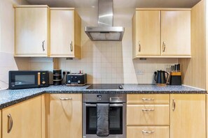 A kitchen with wooden cabinets, a stainless steel range hood, a microwave, a toaster, and a kettle. - Peaceful Redhill House w/ Parking, Near LGW & (Redhill)