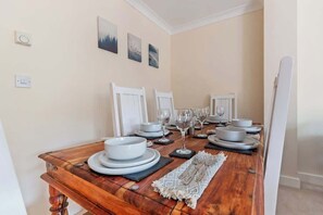 Una mesa de comedor dispuesta con platos, vasos y cubiertos, con un tablero de madera y una silla blanca.