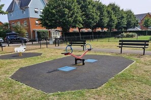 A playground with seesaws and a bench, surrounded by a fence and trees. - Peaceful Redhill House w/ Parking, Near LGW & (Redhill)