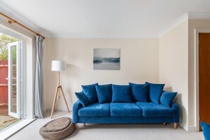 A living room with a blue sofa, a floor lamp, a painting, and a sliding glass door. - Peaceful Redhill House w/ Parking, Near LGW & (Redhill)