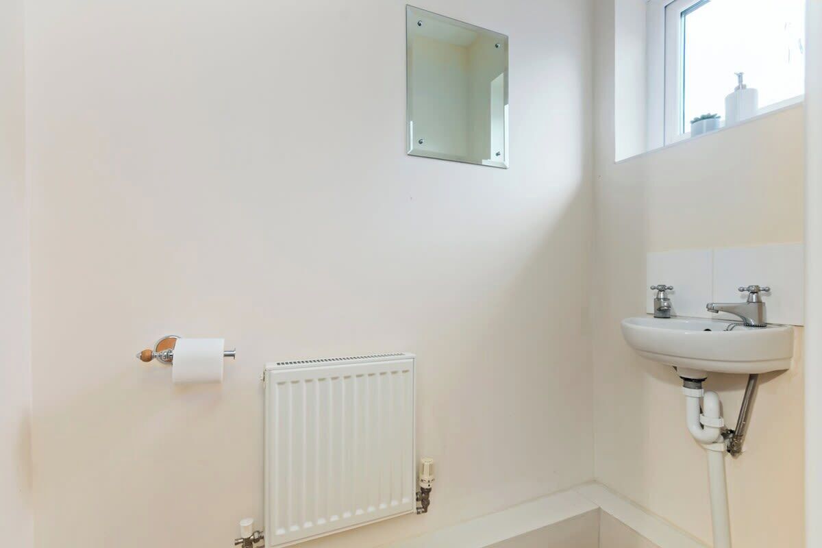 A bathroom with a white radiator, a sink, a mirror, and a toilet paper holder.