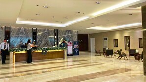 Un área de recepción de hotel moderna con un mostrador de mármol, un panel informativo digital y una zona de estar con sillones.