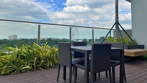 Un balcón con mobiliario de mimbre, vista a una noria y follaje.