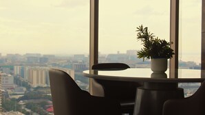 Una mesa redonda con una planta en maceta en el centro, rodeada de sillas, y vistas de la ciudad a través de amplias ventanas.