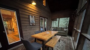 A cozy cabin interior with a wooden dining table, benches, and a sofa.